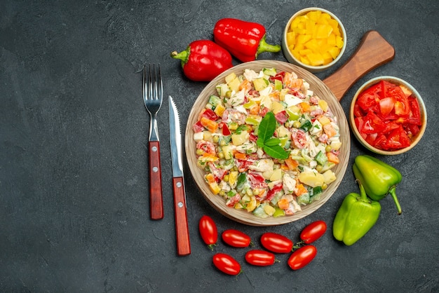 Top view of veggie salad with cutleries and vegetables on side with free place for your text on dark grey background