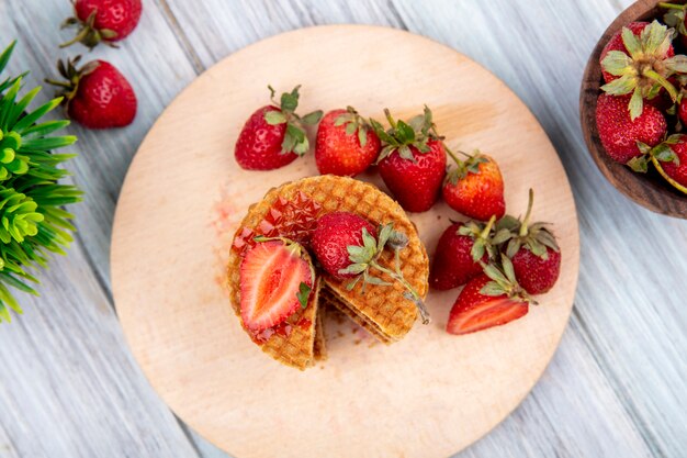 Top view of waffle biscuits and strawberries in plate and bowl and on wooden surface