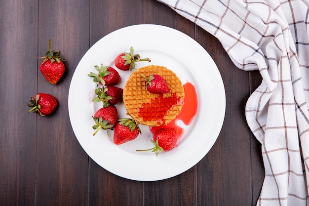 Free Photo top view of waffle biscuits and strawberries in plate with plaid cloth on wooden surface