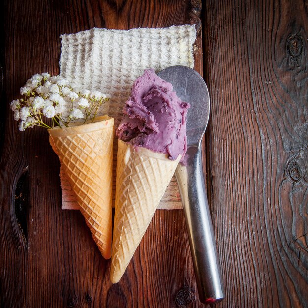 Top view waffle cones with blueberry ice cream and gypsophila and ice cream spoon in rag napkins