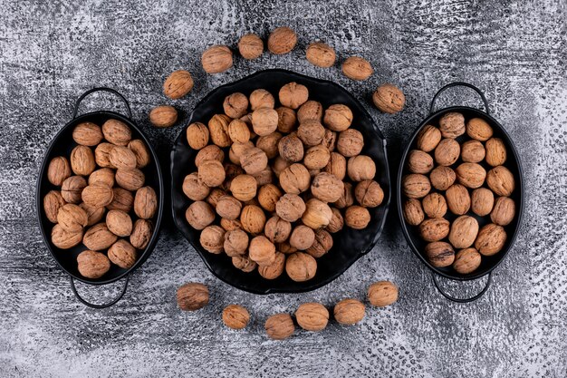 Top view walnuts in black baskets and plate on wooden table horizontal