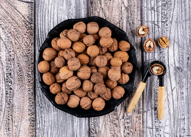 Top view walnuts in black plate with nutcracker on wooden  horizontal