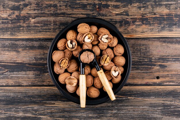 Top view walnuts and nutcracker in plate on wooden table horizontal