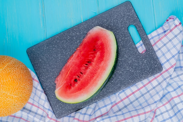 Free Photo top view of watermelon slice on cutting board with whole melon on plaid cloth and blue background