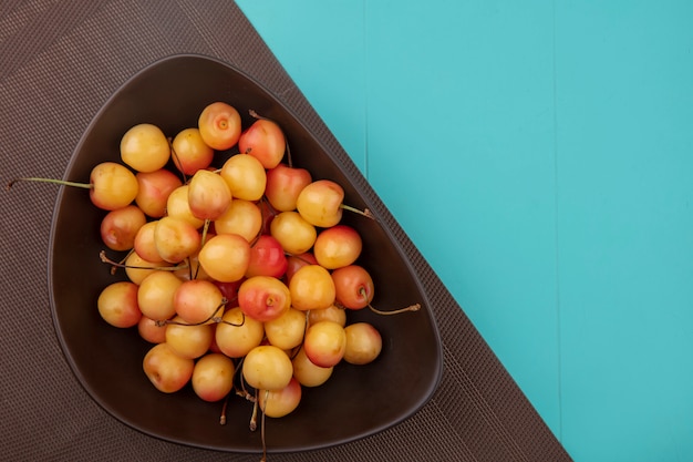 Top view white cherry in a bowl on a brown towel on a turquoise table