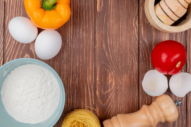 Top view of white chicken eggs with flour on a blue bowl with egg shells with a tomato on a wooden background with copy space