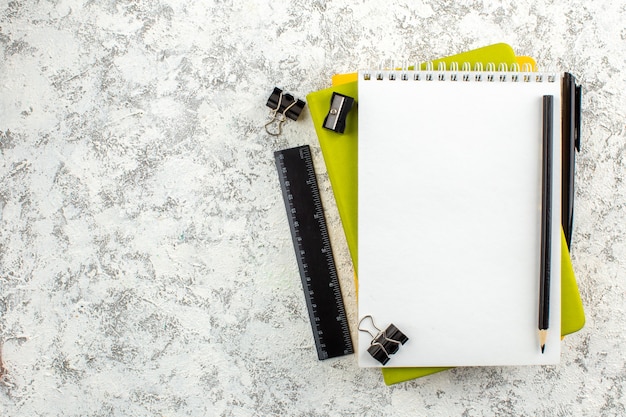 Top view of white closed spiral notebook and office supplies on the left side on white background