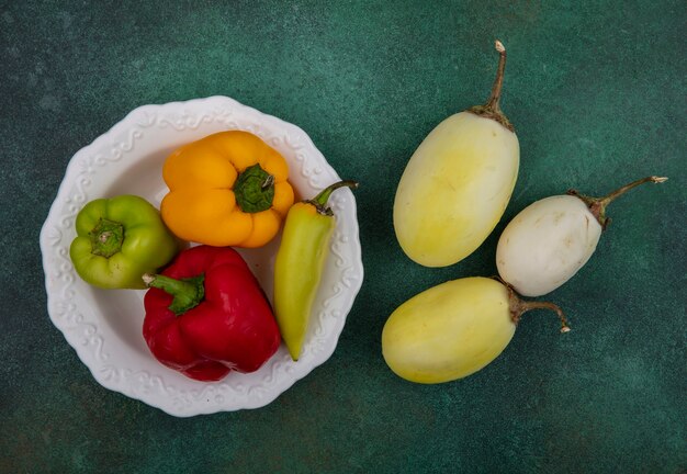 Top view white eggplant with bell peppers on a plate on a green background