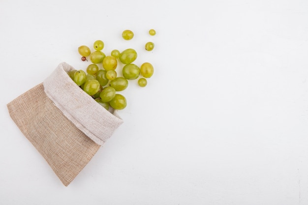 Top view of white grape berries spilling out of sack on white background with copy space