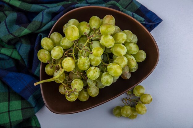 Top view of white grape in bowl on plaid cloth and on gray background