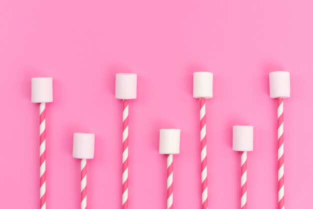 A top view white marshmallows with pink sticks on pink desk, sugar sweet color