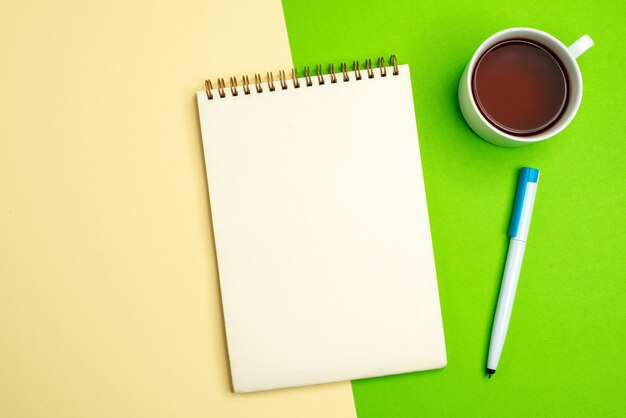 Free Photo top view of white notebook with pen next to a cup of tea on white and yellow background