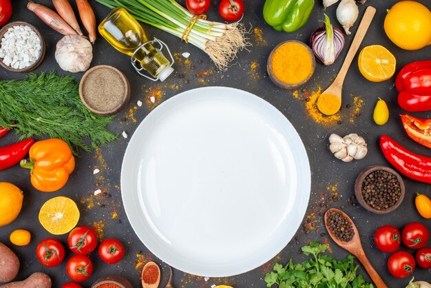 Top view white round plate black pepper turmeric and sea salt in small bowls garlic tomatoes coriander dill green onions oil bottle on table