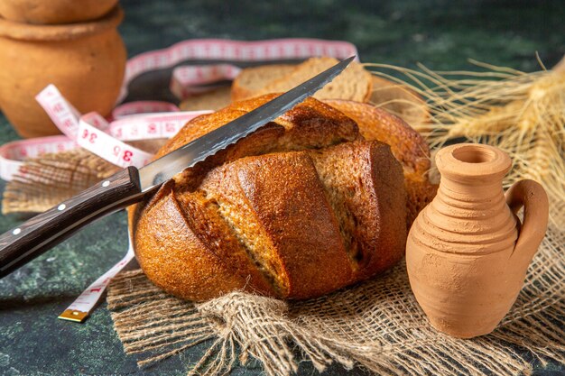 Top view of whole and cut black bread and spikes on brown towel meter potteries on dark colors surface