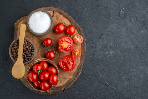 Top view of whole cut fresh tomatoes and pepper on wooden board on black surface