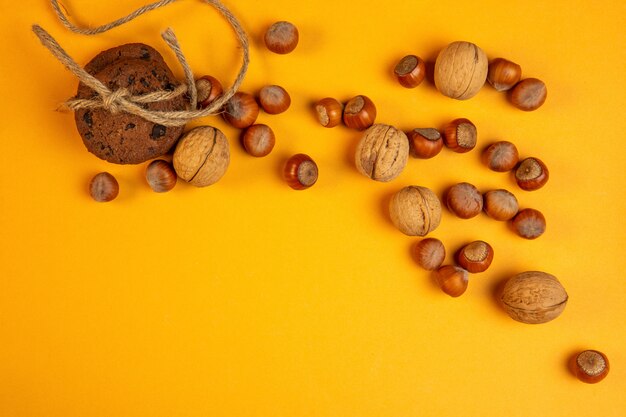 Top view of whole walnuts and hazelnuts and oatmeal cookies tied with rope on yellow