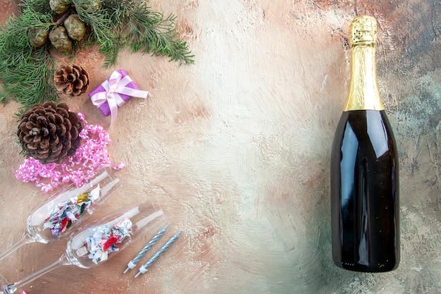 Top view wine glasses with little presents and bottle of champagne on light background