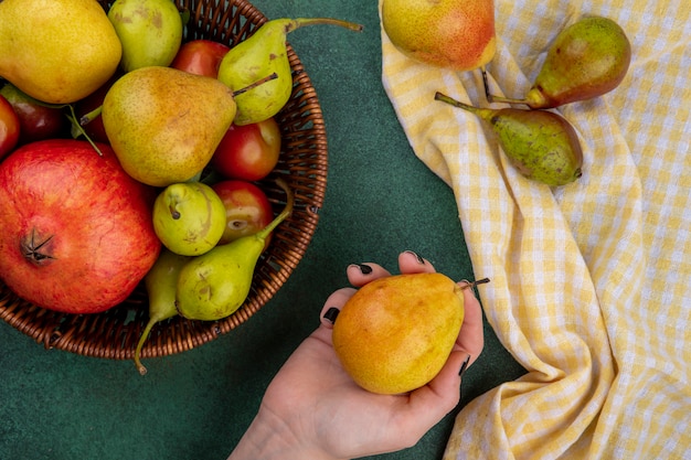 Free Photo top view of woman hand holding peach with basket of pomegranate peach plum on green surface