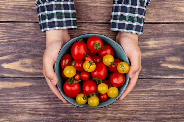 Free photo top view of woman hands holding bowl of tomatoes on wooden table