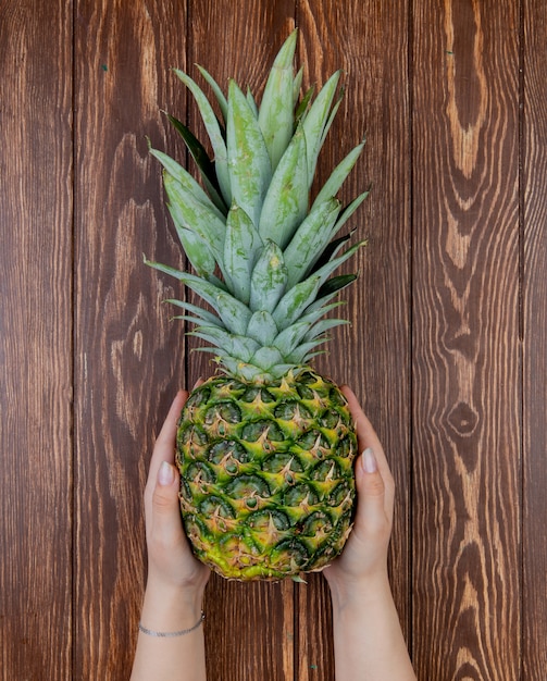 Free photo top view of woman hands holding pineapple on wooden table