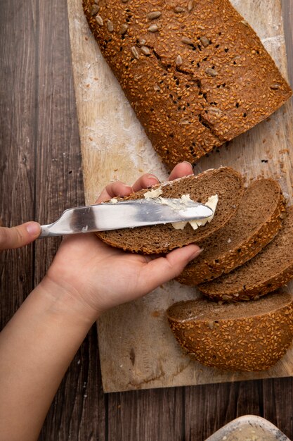 Top view of woman hands spreading butter on bread and bread slices on wooden surface and background