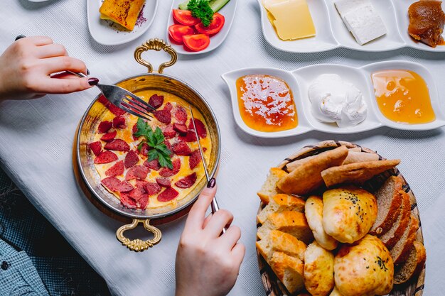 Top view a woman having breakfast omelet with sausage in a pan with a basket of bread