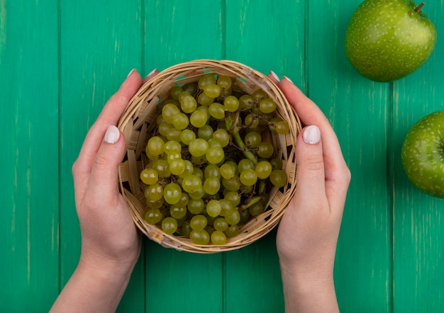 Free photo top view  woman holding green grapes in a basket with green apples on a green background