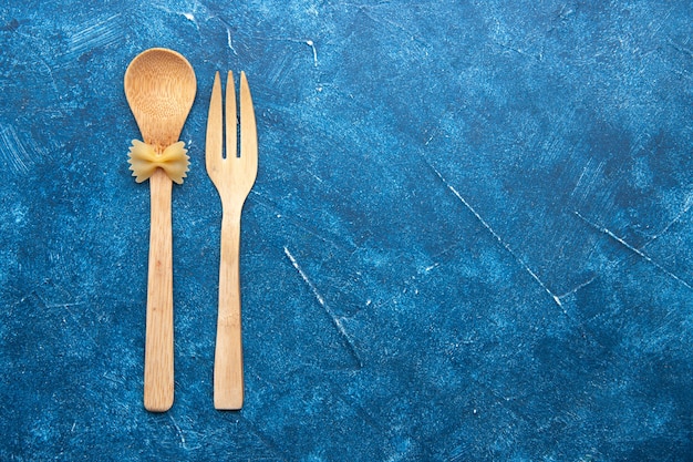 Free photo top view wooden fork spoon farfalle on spoon on blue table with free space