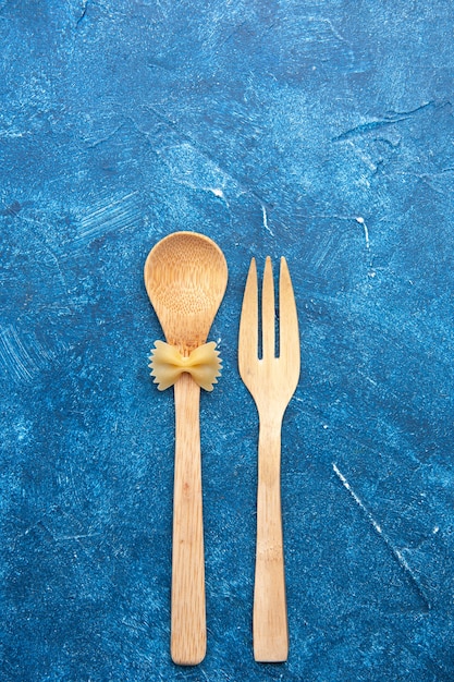 Free photo top view wooden fork spoon farfalle on spoon on blue table with free space