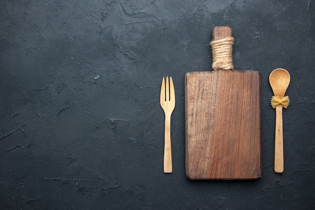 Top view wooden serving board wooden spoon and fork on dark table copy place