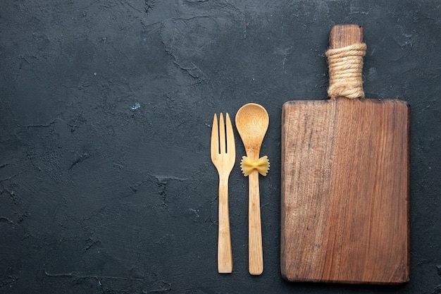 Free photo top view wooden serving board wooden spoon and fork on dark table copy space