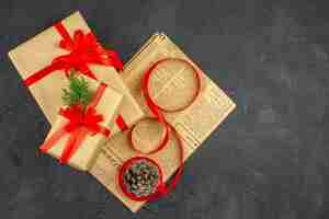 Free photo top view xmas gift in brown paper branch fir ribbon on newspaper pinecone on dark surface