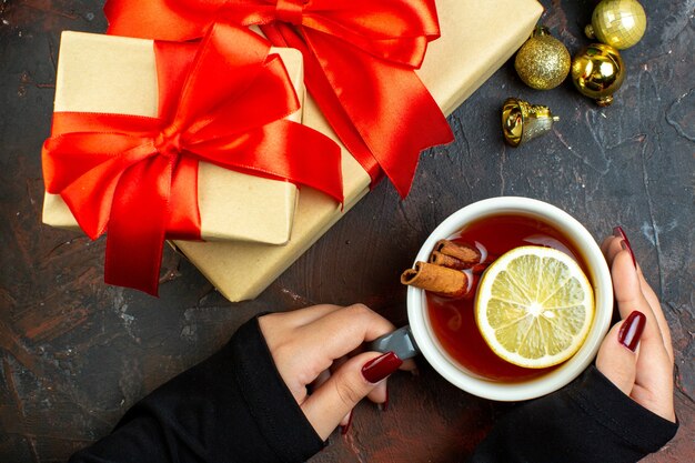 Top view xmas gifts golden xmas balls cup of tea in female hand on dark red table