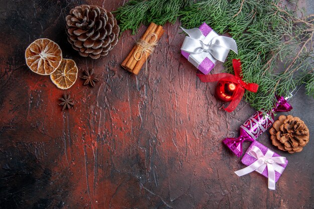 Top view xmas gifts pine tree branches with cone xmas tree toys cinnamon dried lemon slices anises on dark red surface