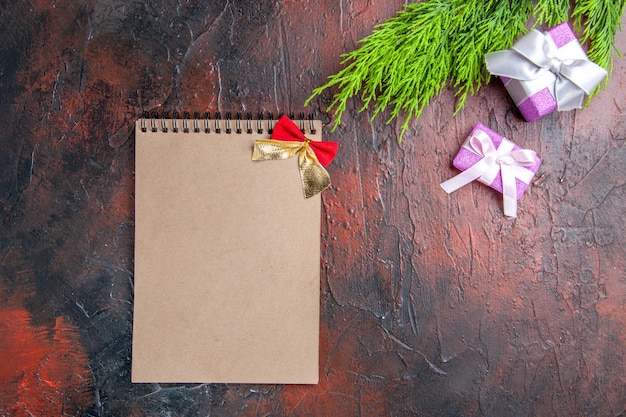 Top view xmas gifts with pink box and white ribbon tree branch a notebook on dark red background