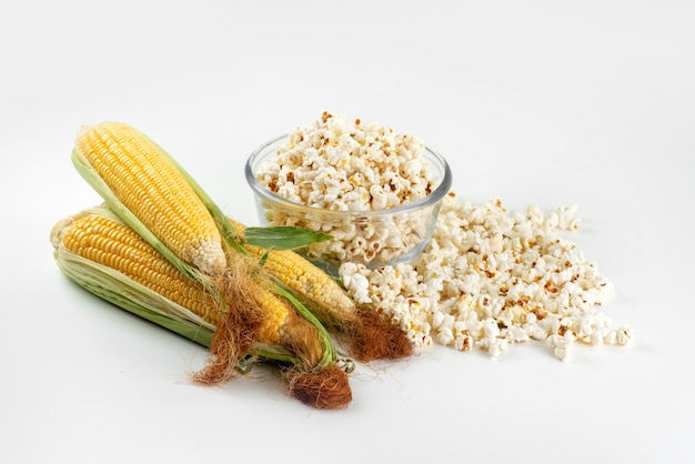 Free photo a top view yellow corns raw with green leaves and fresh popcorn on white desk, food meal color corn