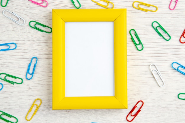 Top view of yellow empty picture frame and paper clips on white wooden stripped