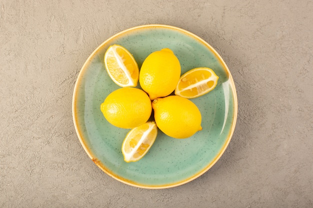 Free photo a top view yellow fresh lemons ripe mellow and juicy whole and sliced inside green plate on the grey background fruits citrus color