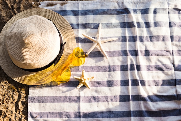 Free photo top view of yellow heart sunglasses, straw hat and starfish on beach towel at beach