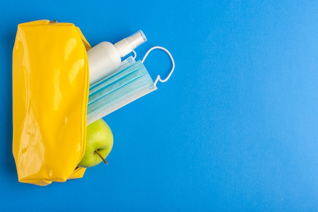 Top view yellow pen box with spray apple and mask on blue surface