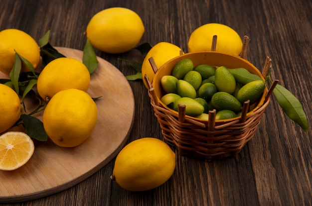 Top view of yellow skinned lemons isolated on a wooden kitchen board with kinkans on a bucket on a wooden wall