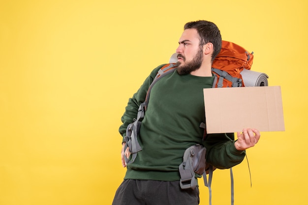 Free photo top view of young angry travelling guy with backpack holding a sheet without writing on yellow