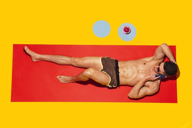 Free photo top view of young caucasian male model's resting on beach resort on red mat and yellow