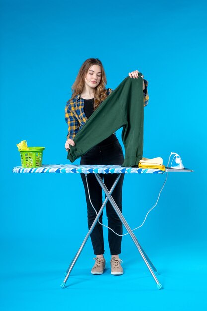 Top view of young female holding the blouse standing behind the ironing board in the laundry room 