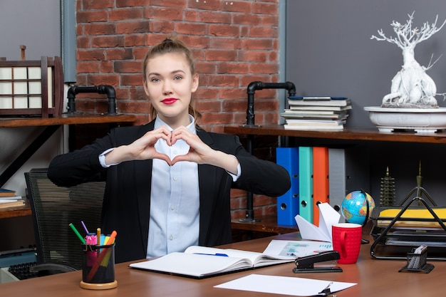 Free photo top view of young female sitting at a table and making heart gesture in the office