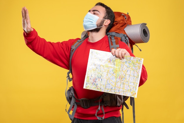 Top view of young proud traveller guy wearing medical mask with backpack holding map on yellow