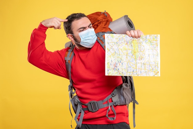 Free photo top view of young thinking traveller guy wearing medical mask with backpack holding map on yellow