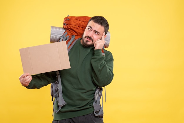 Free Photo top view of young thinking travelling guy with backpack holding a sheet without writing on yellow