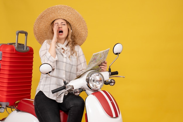 Top view of young woman wearing hat and sitting on motorcycle and holding map calling someone on yellow 