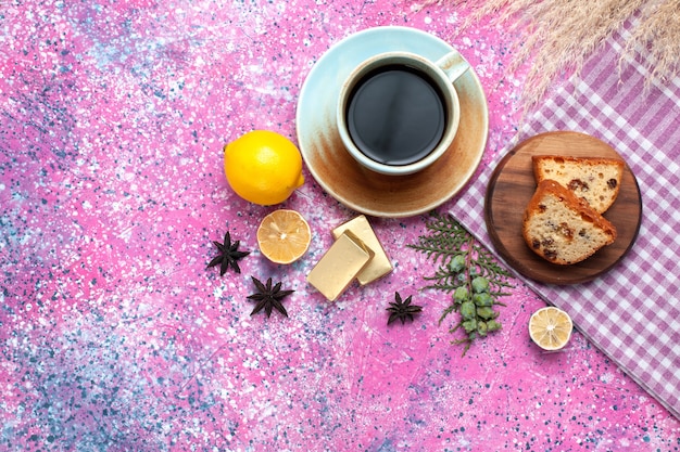 Top view of yummy cake sliced with cup of tea and lemons on light pink surface